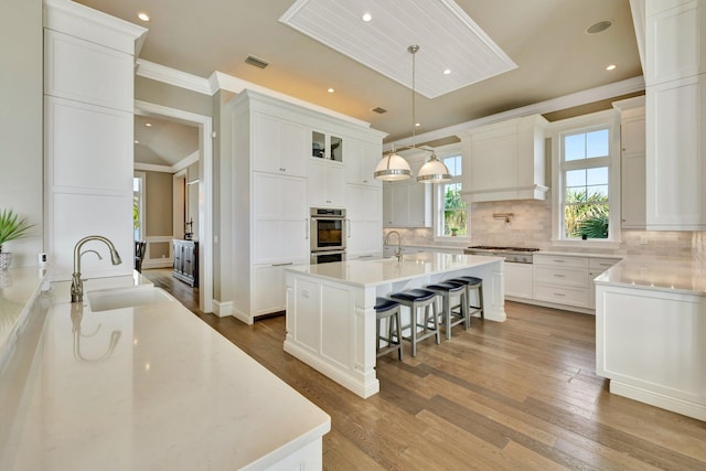 kitchen with a sink, wood finished floors, an island with sink, and backsplash