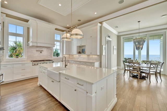 kitchen featuring stainless steel gas cooktop, light countertops, light wood-style floors, ornamental molding, and a sink