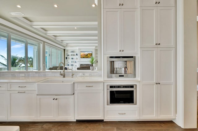 kitchen featuring white cabinets, stainless steel oven, beamed ceiling, and a sink