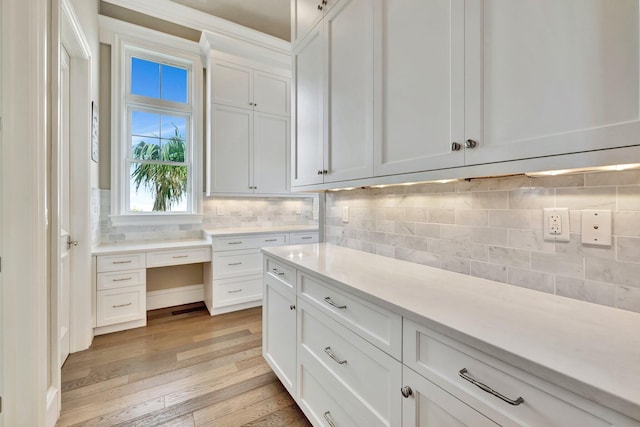 kitchen with light wood-type flooring, white cabinets, light countertops, and backsplash