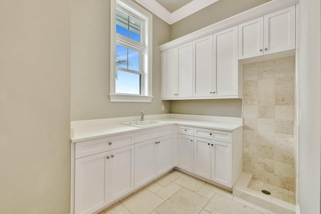 kitchen with stone tile floors, a sink, white cabinetry, light countertops, and crown molding