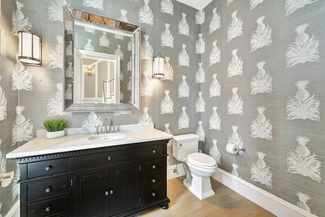 half bath with toilet, wallpapered walls, wood finished floors, and vanity