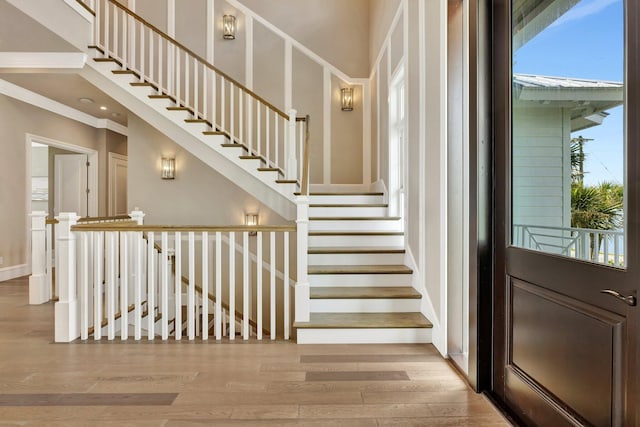 stairway featuring baseboards, a high ceiling, wood finished floors, and a healthy amount of sunlight