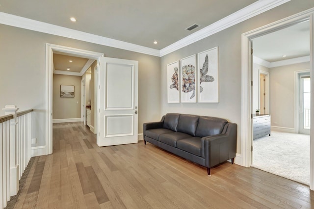 sitting room with ornamental molding, light wood-type flooring, visible vents, and baseboards