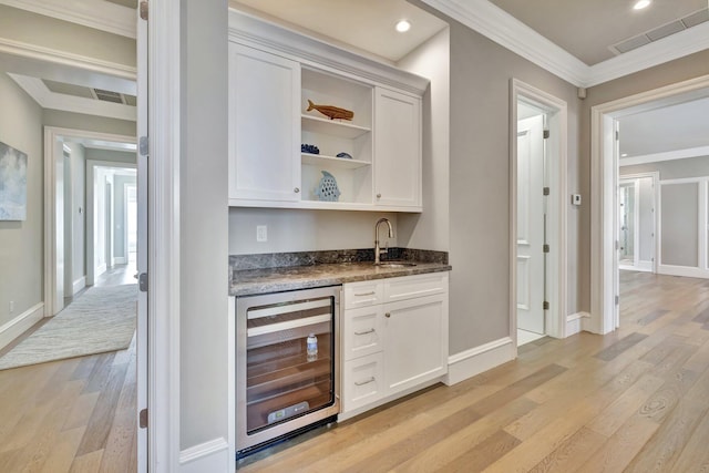 bar with beverage cooler, a sink, visible vents, ornamental molding, and light wood finished floors