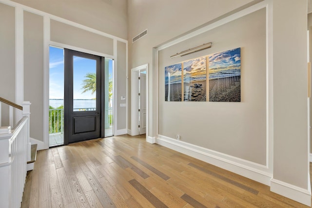 entrance foyer with light wood finished floors, baseboards, visible vents, a towering ceiling, and stairs