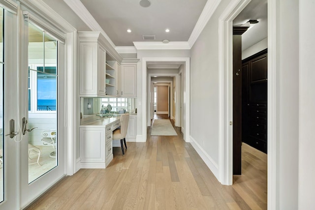 corridor with light wood-type flooring, visible vents, baseboards, and crown molding