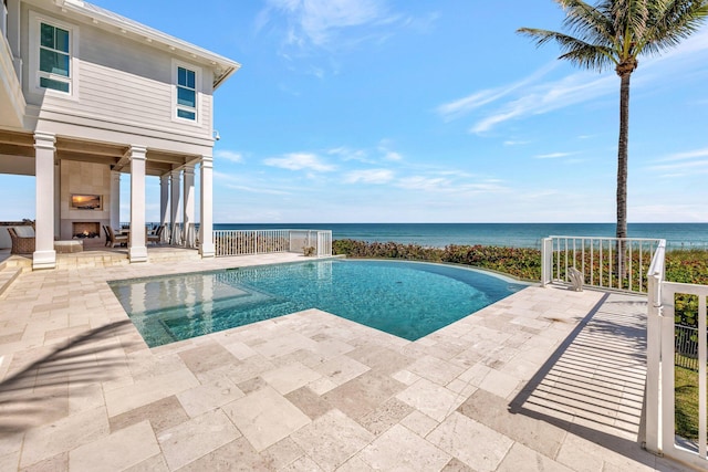 view of pool with an infinity pool, exterior fireplace, a water view, a patio area, and fence