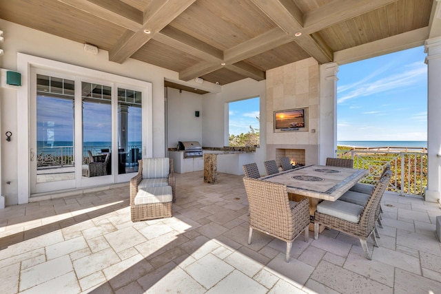 view of patio with a water view, a large fireplace, a grill, and exterior kitchen