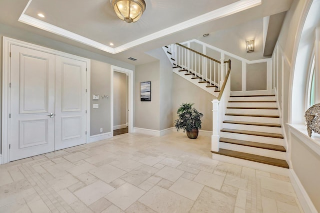 foyer with stone tile floors, baseboards, visible vents, ornamental molding, and a tray ceiling