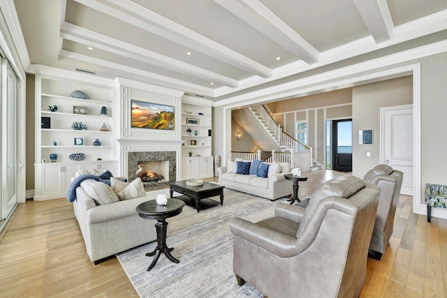 living area with a fireplace, stairs, light wood-type flooring, beamed ceiling, and crown molding