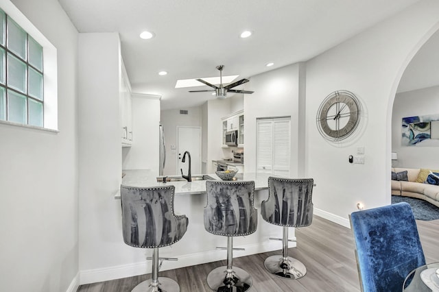 kitchen featuring a kitchen bar, wood-type flooring, appliances with stainless steel finishes, light stone counters, and white cabinets