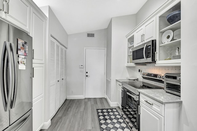 kitchen with white cabinets, appliances with stainless steel finishes, light stone counters, and light hardwood / wood-style flooring