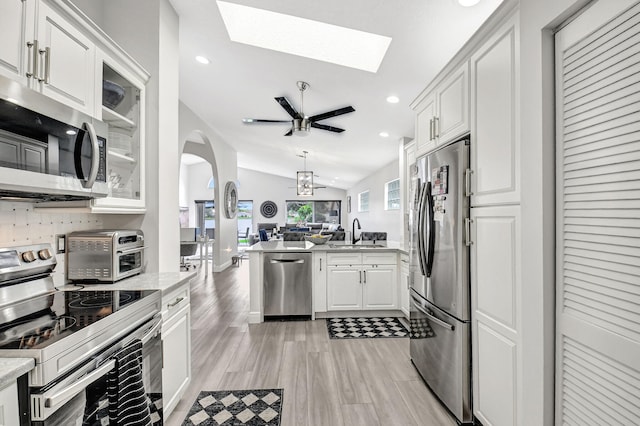 kitchen featuring white cabinetry, lofted ceiling, light stone countertops, sink, and appliances with stainless steel finishes