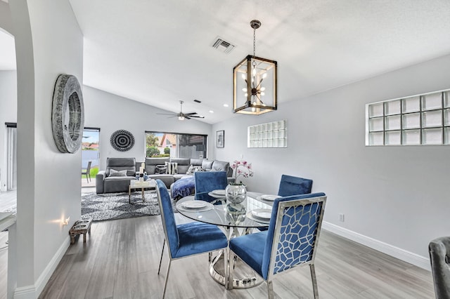 dining space with ceiling fan with notable chandelier, vaulted ceiling, and hardwood / wood-style floors