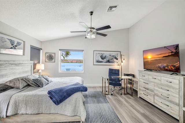 bedroom featuring ceiling fan, light wood-type flooring, vaulted ceiling, and a textured ceiling