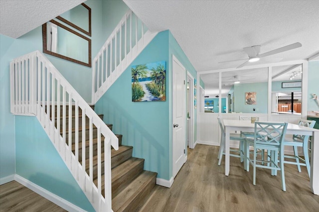 stairs with ceiling fan, wood-type flooring, and a textured ceiling