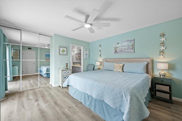 bedroom featuring ceiling fan, ensuite bath, light hardwood / wood-style floors, and a textured ceiling