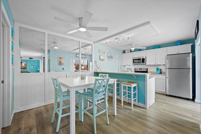 dining area featuring ceiling fan, sink, light hardwood / wood-style floors, and a textured ceiling