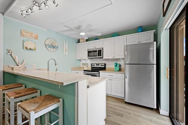 kitchen featuring appliances with stainless steel finishes, a kitchen breakfast bar, kitchen peninsula, ceiling fan, and white cabinets