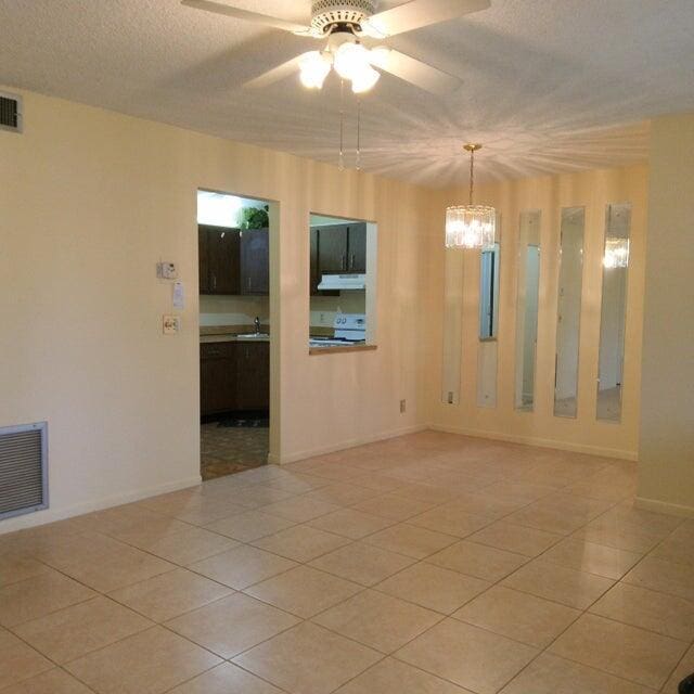 spare room featuring light tile patterned floors, a textured ceiling, ceiling fan with notable chandelier, and visible vents