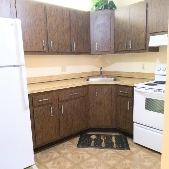 kitchen featuring white appliances, range hood, light countertops, and a sink