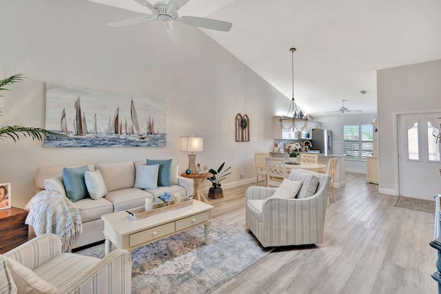 living room with ceiling fan with notable chandelier, high vaulted ceiling, and light hardwood / wood-style floors