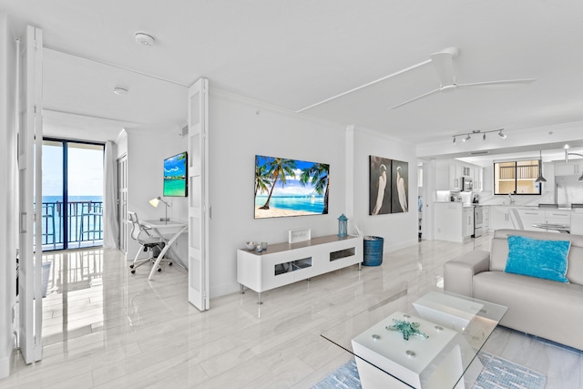 living area with baseboards, rail lighting, a ceiling fan, and crown molding