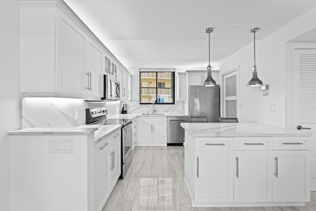 kitchen featuring appliances with stainless steel finishes, light stone countertops, white cabinetry, pendant lighting, and a sink