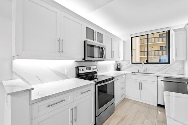 kitchen with a sink, white cabinetry, decorative backsplash, stainless steel appliances, and light stone countertops