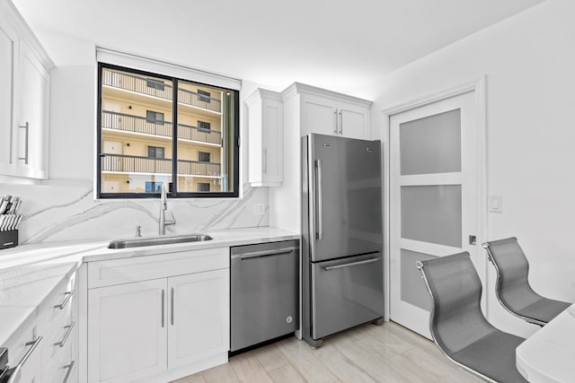 kitchen with appliances with stainless steel finishes, a sink, white cabinetry, and light stone countertops