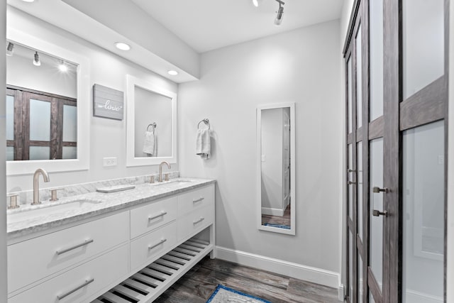 bathroom with a sink, wood finished floors, baseboards, and double vanity