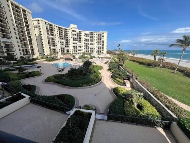 view of community with a water view, a yard, a patio area, a pool, and a view of the beach