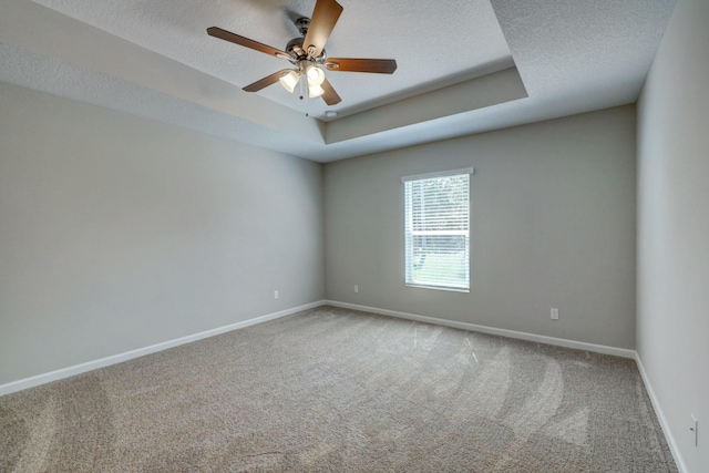 carpeted empty room featuring ceiling fan, a raised ceiling, and a textured ceiling