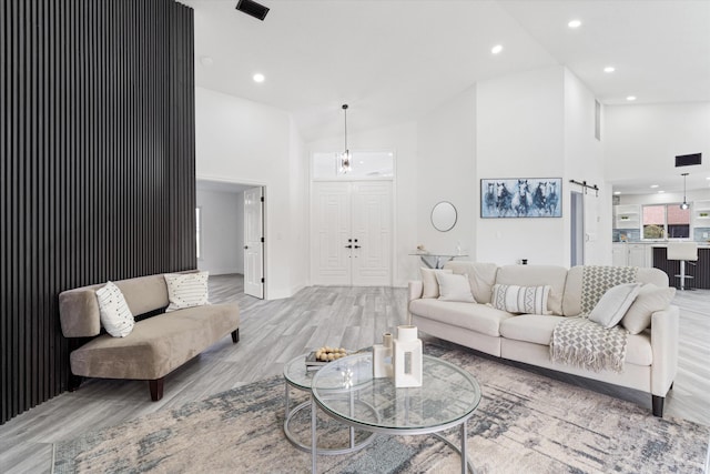 living room featuring high vaulted ceiling, a barn door, and light wood-type flooring