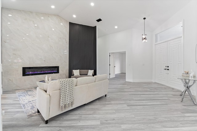 living room with high vaulted ceiling, a high end fireplace, and light hardwood / wood-style floors