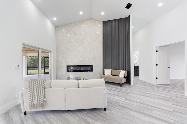 living room with a high end fireplace, light hardwood / wood-style floors, and high vaulted ceiling