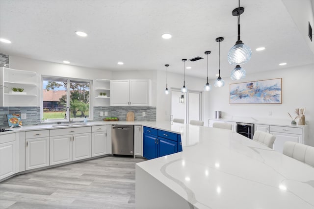 kitchen featuring pendant lighting, sink, blue cabinetry, light stone counters, and white cabinets