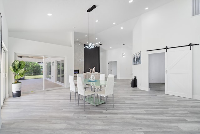 unfurnished dining area with high vaulted ceiling, a barn door, and light hardwood / wood-style floors