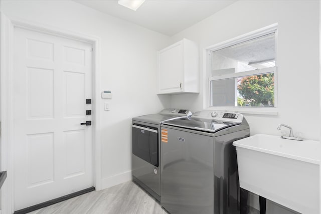 laundry area featuring cabinets, sink, washer and dryer, and light wood-type flooring