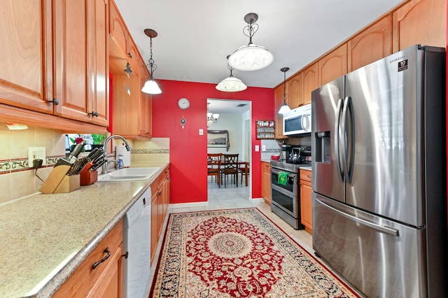kitchen featuring stainless steel appliances, a sink, pendant lighting, decorative backsplash, and baseboards