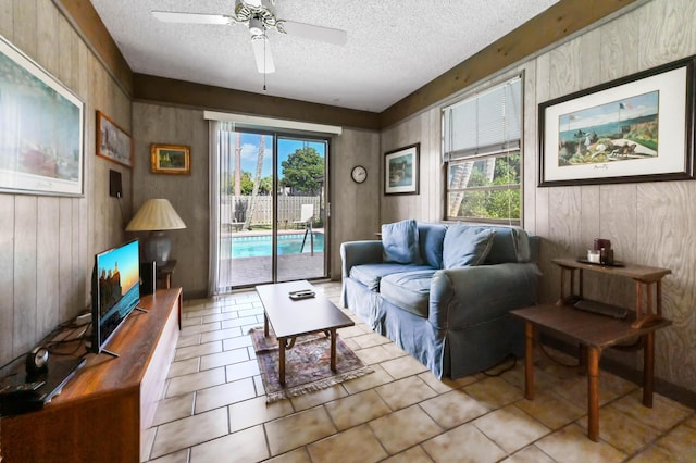 tiled living room with wooden walls, a textured ceiling, and a ceiling fan