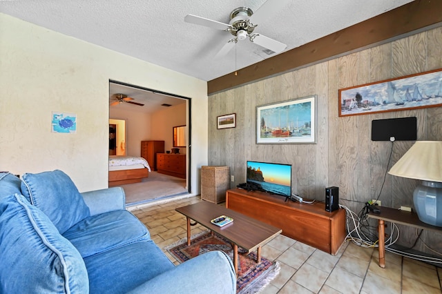 living area featuring wooden walls, a textured ceiling, and a ceiling fan