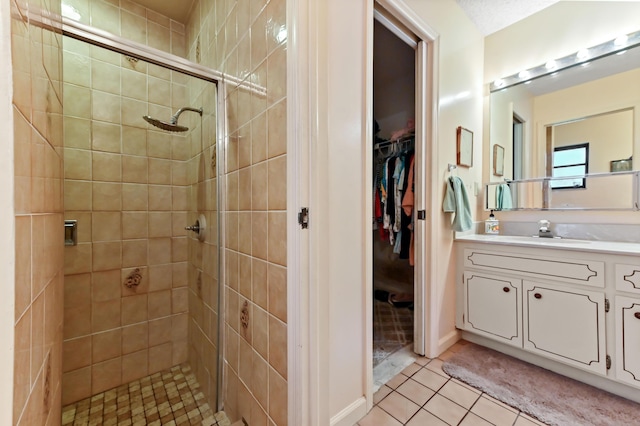 bathroom with tile patterned floors, vanity, a walk in closet, and a tile shower