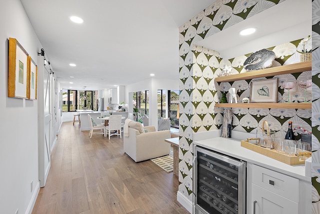 bar featuring wood-type flooring, beverage cooler, white cabinets, and a barn door