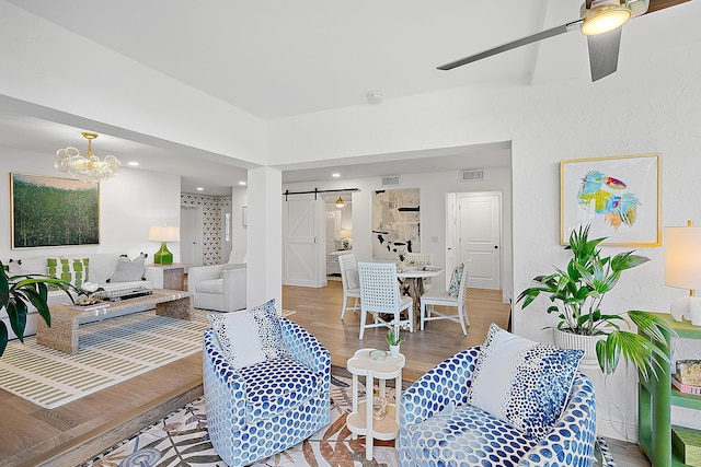 living room featuring hardwood / wood-style flooring, a barn door, and ceiling fan with notable chandelier