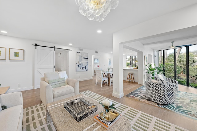 living room featuring ceiling fan with notable chandelier, a barn door, and hardwood / wood-style floors