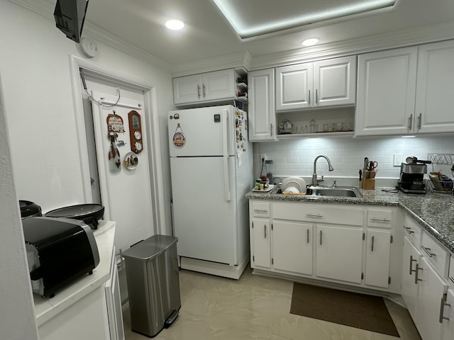 kitchen with white refrigerator, tasteful backsplash, sink, and white cabinets