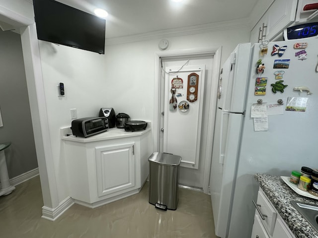 kitchen featuring white refrigerator, dark stone counters, crown molding, and white cabinets