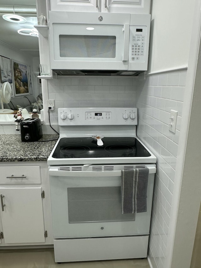 kitchen featuring white appliances, tile walls, backsplash, white cabinets, and dark stone counters